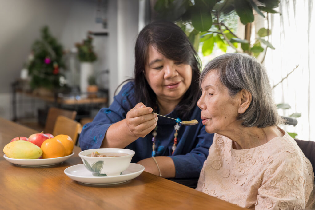 Adult giving senior a spoonful of food