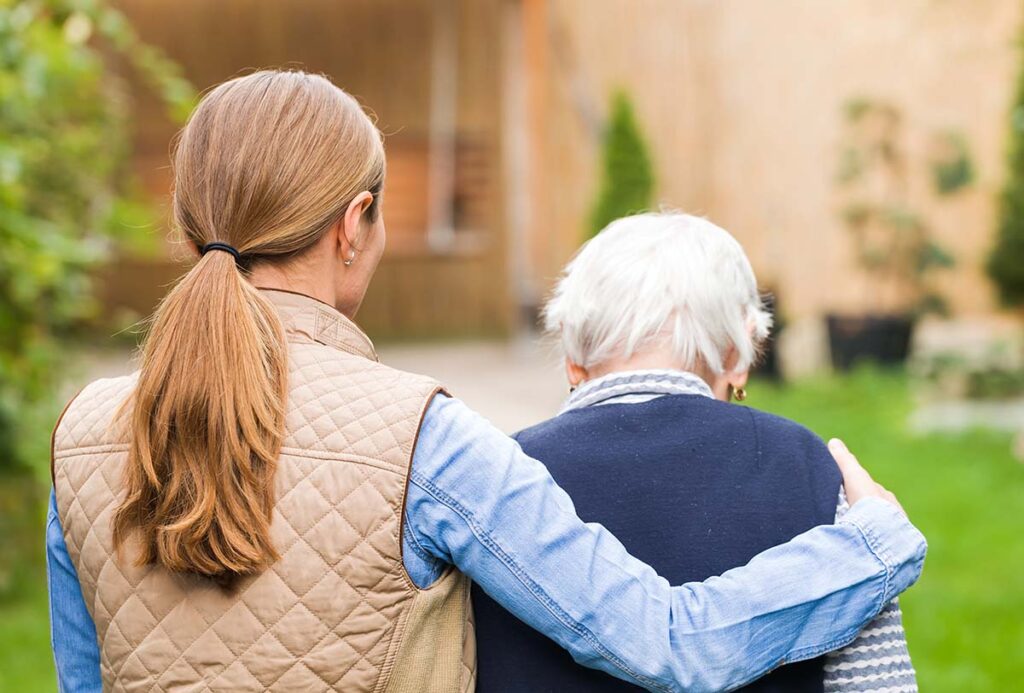 person who is part of sandwich generation​ with arm around older loved one while walking outdoors