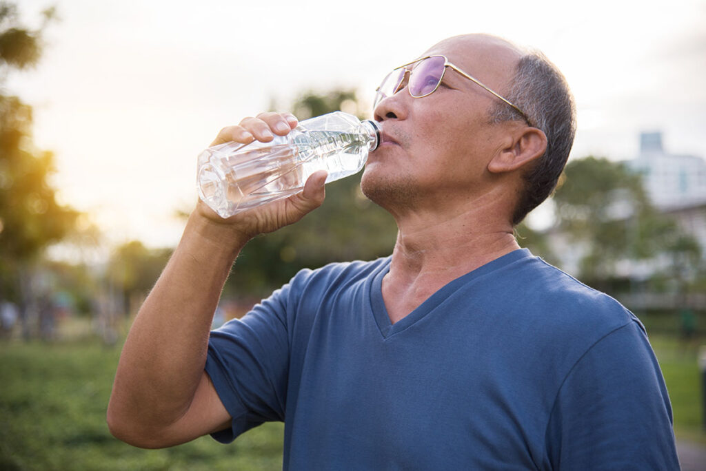 person drinking water outdoors after learning about dehydration in seniors​