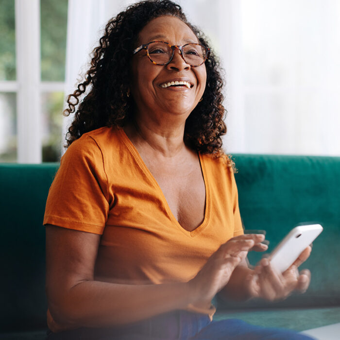 a smiling senior woman plays with her phone on the couch