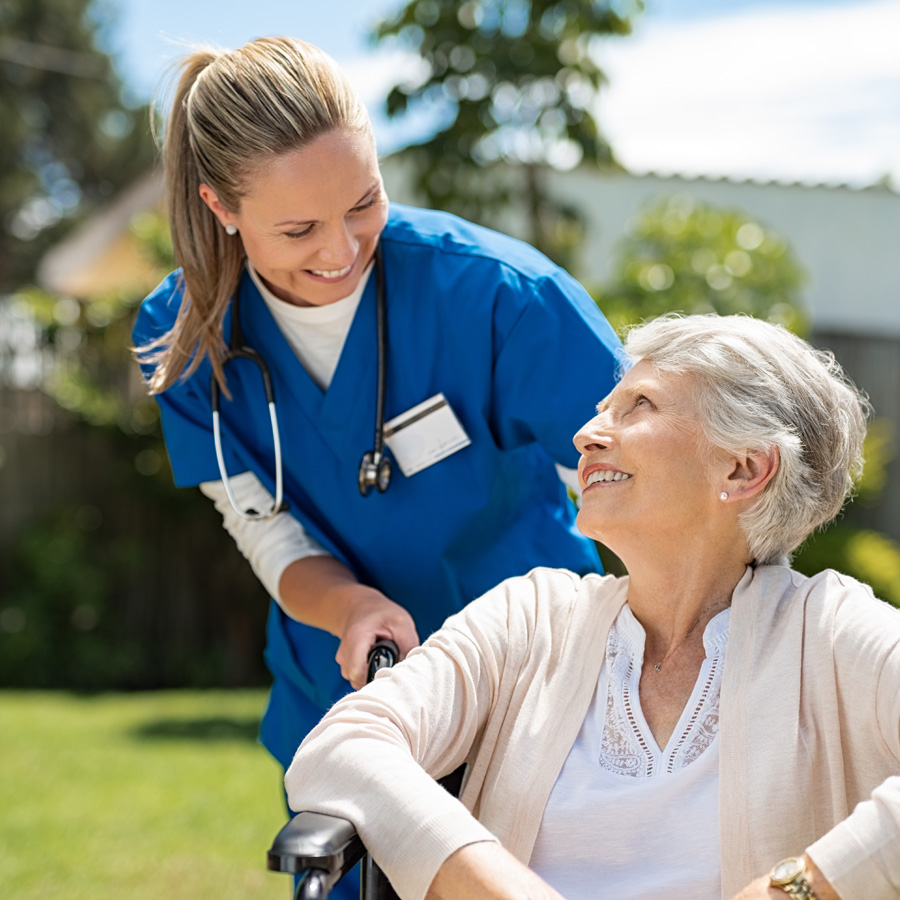 a senior woman in a wheelchair gets assistance outside from a cna