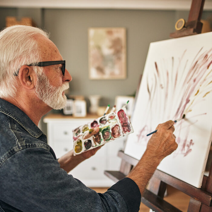 a senior man works on a painting in his apartment in senior living