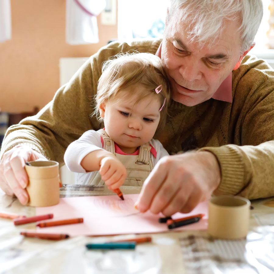 a senior man colors a picture with his toddler granddaughter