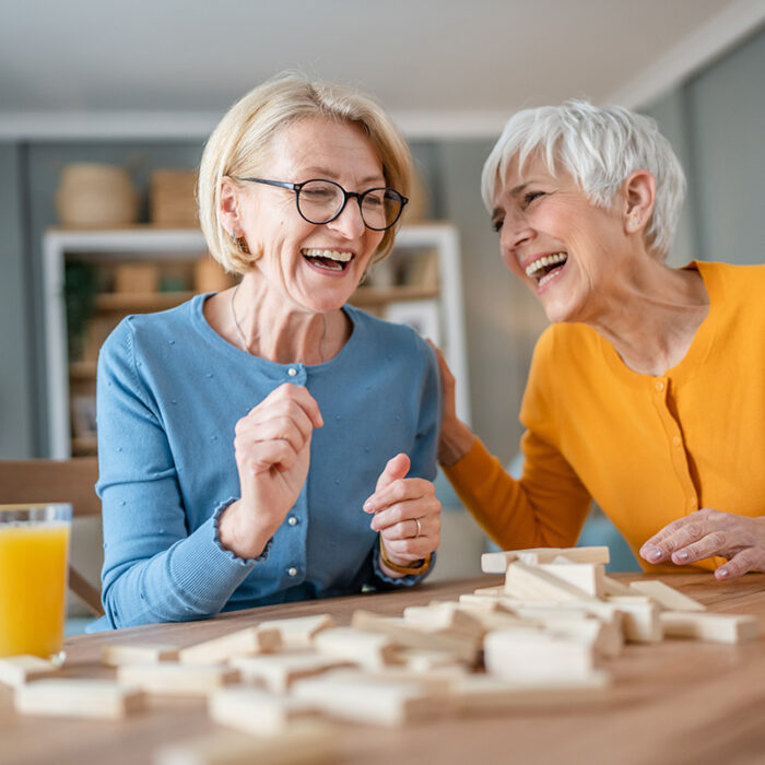 two senior women laugh together while playing jenga